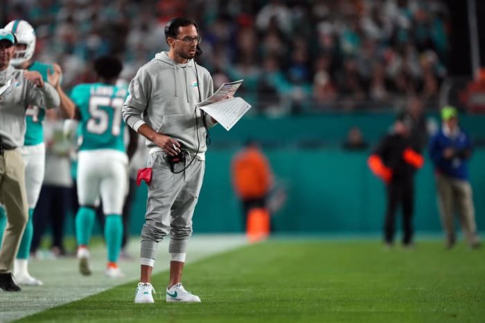 Mike McDaniel stands on the sideline looking at a piece of paper